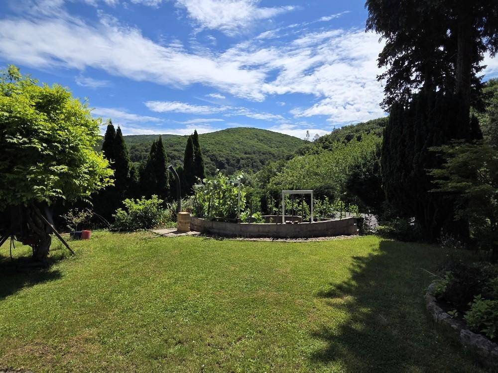 Sonnige Rasenfläche im Garten mit Blick auf die umliegenden bewaldeten Hügel.