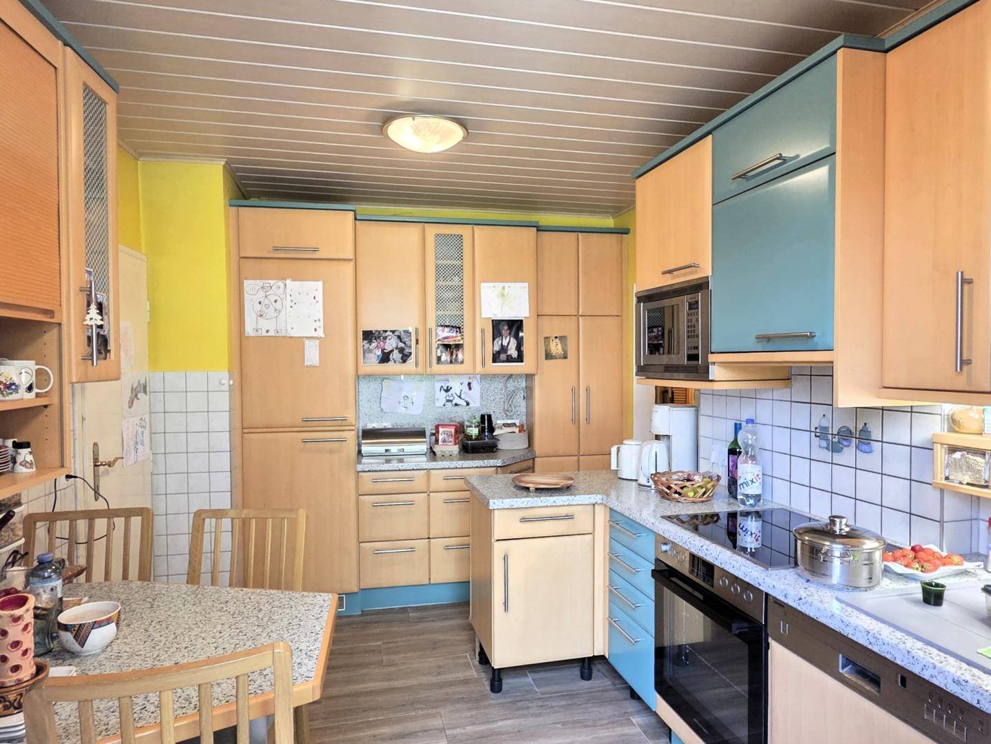 Funktionale Küche mit hellen Holzschränken, blauen Akzenten und Essbereich.