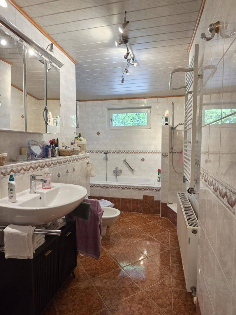 Gefliestes Badezimmer mit Badewanne, Dusche, Doppelwaschbecken und Fenster.