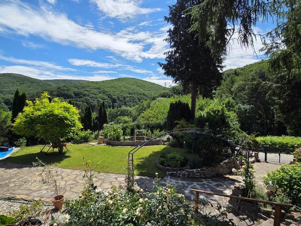 Weitläufiger Garten mit Rasenfläche, Steinplatten und Panoramablick auf bewaldete Hügel.