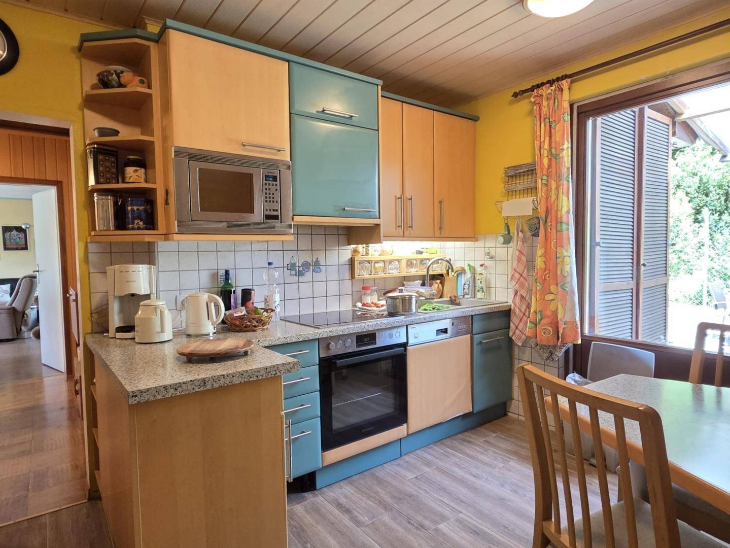 Helle Küche mit Holz- und blauen Fronten, integrierten Geräten und Fenster zum Garten.