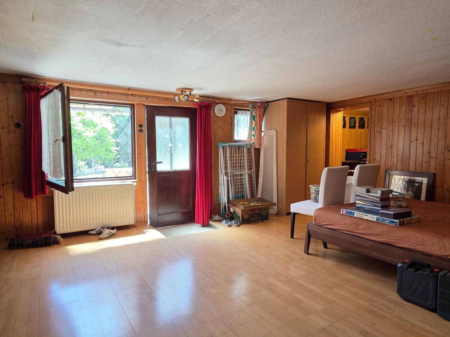 Helles Zimmer mit Holzboden, Holzvertäfelung und Zugang zum Außenbereich.