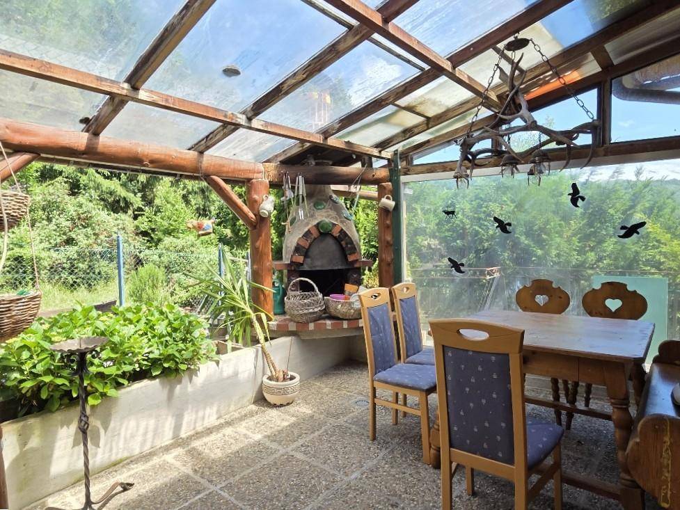 Verglaster Wintergarten mit Essbereich, Außenkamin und Blick ins Grüne.