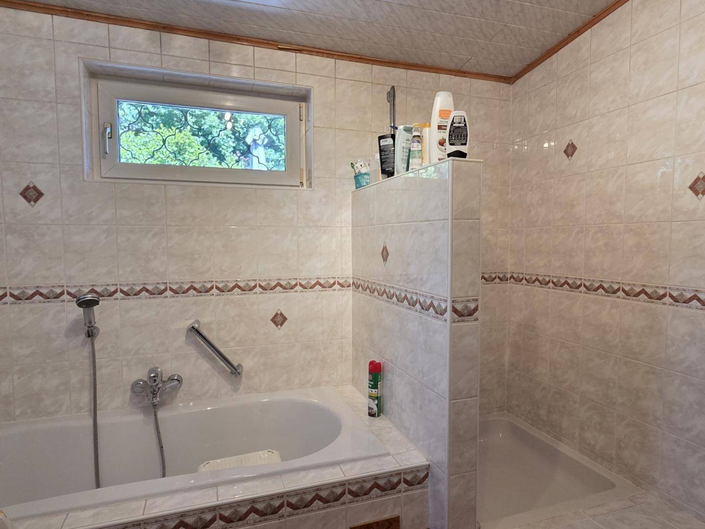 Gefliestes Badezimmer mit Badewanne, Duschbereich und Fenster.