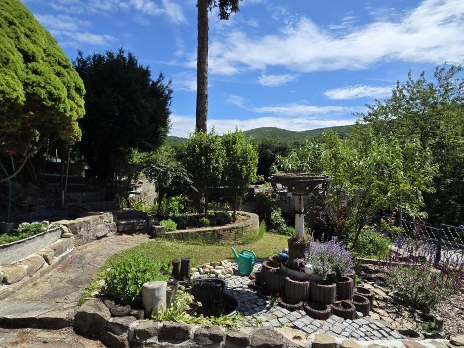 Kreativ gestalteter Gartenbereich mit kleinen Teichen, Pflanzen und Blick auf die Landschaft.
