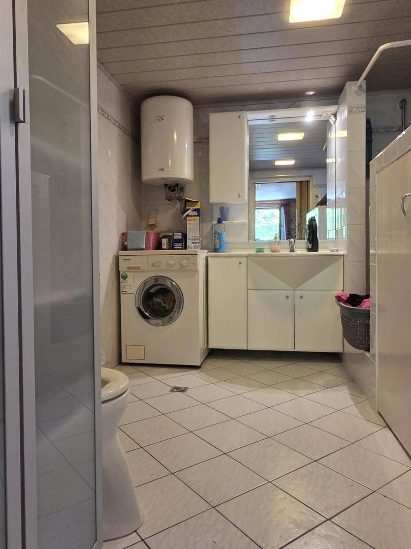 Funktionales Badezimmer mit Waschmaschine, Waschbecken und Spiegelschrank, gefliestem Boden.