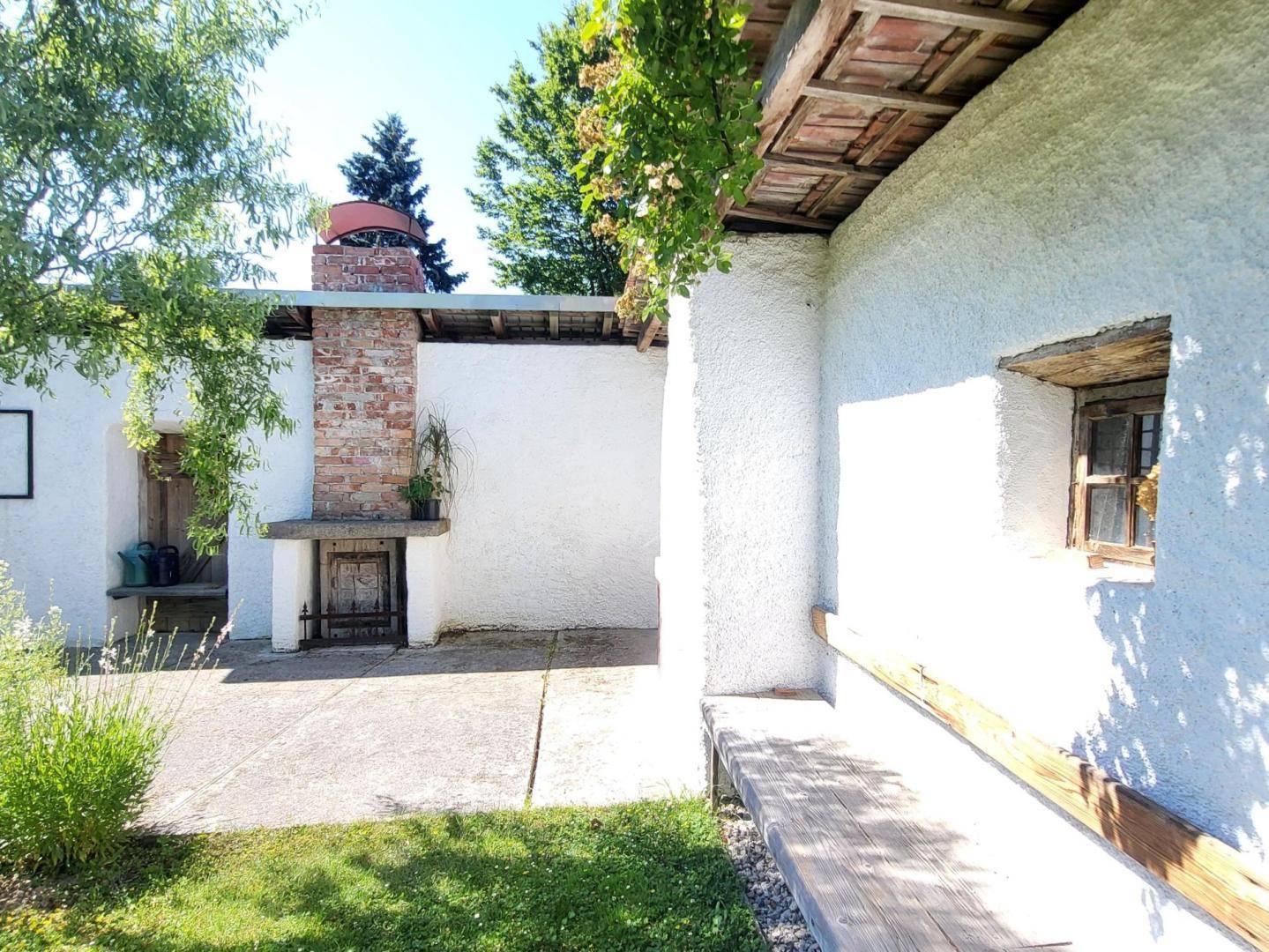 Weißes Gebäude mit Ziegelkamin und gepflastertem Terrassenbereich, ergänzt durch eine Holzbank.