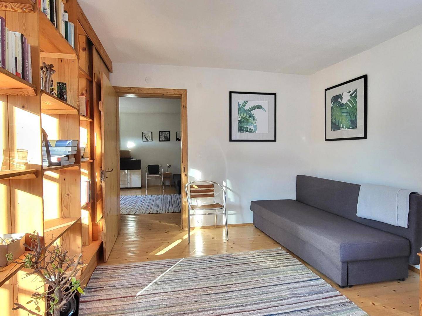 Heller Raum mit Holzbücherregal, Sofa und Teppich, durchflutet von natürlichem Sonnenlicht.