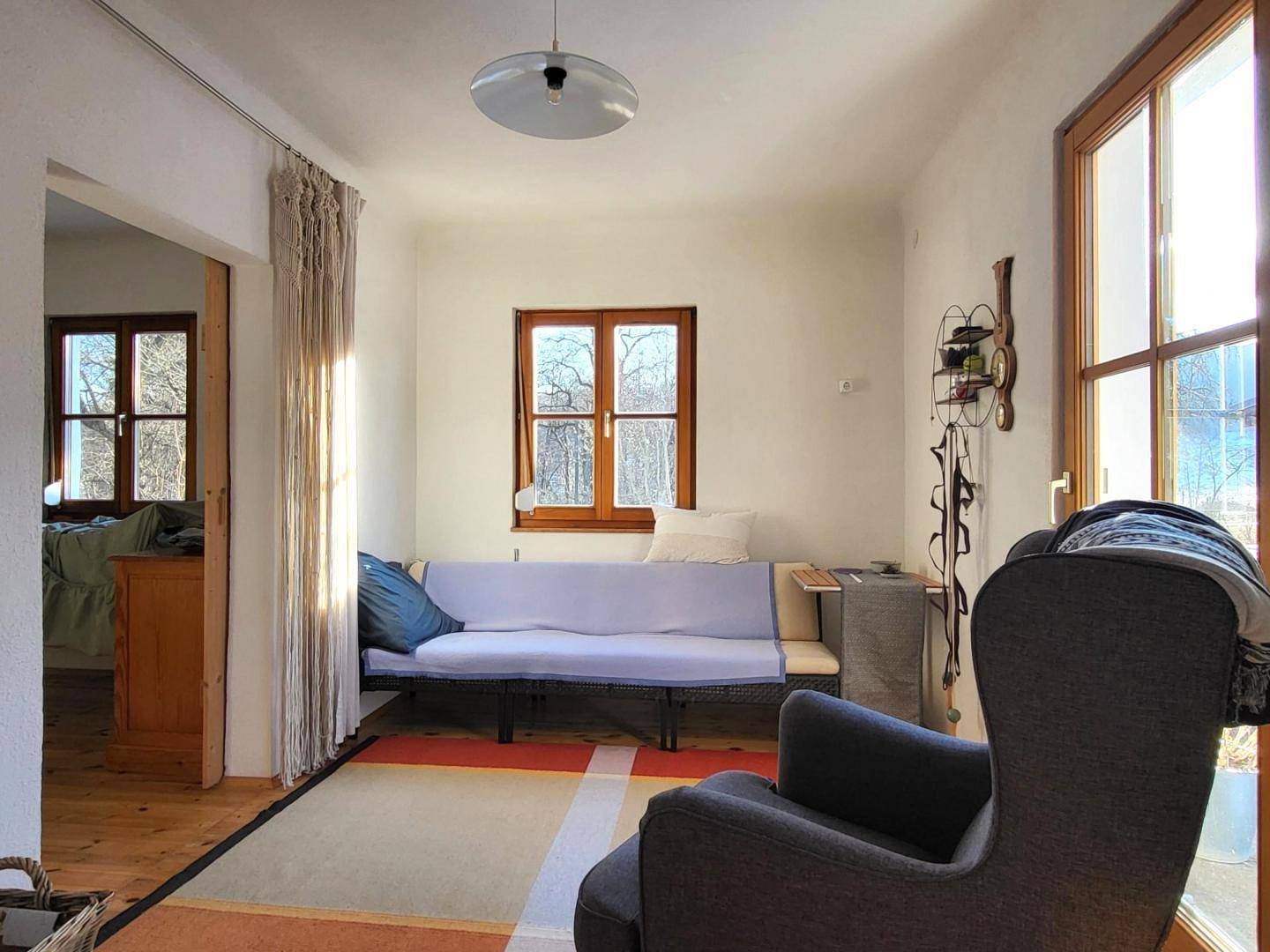 Helles Wohnzimmer mit beigem Sofa, Holzboden und großen Fenstern, die viel Sonnenlicht hereinlassen.