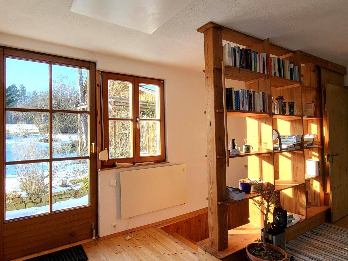 Heller Raum mit großen Holzfenstern und Bücherregal, bietet Blick auf eine winterliche Landschaft.