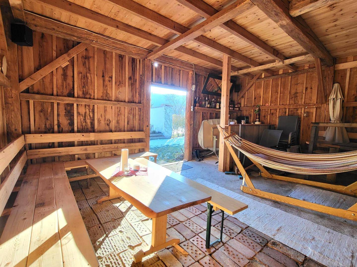 Rustikaler Holzschuppen, umgebaut zu einem geselligen Raum mit langem Tisch und Hängematte.