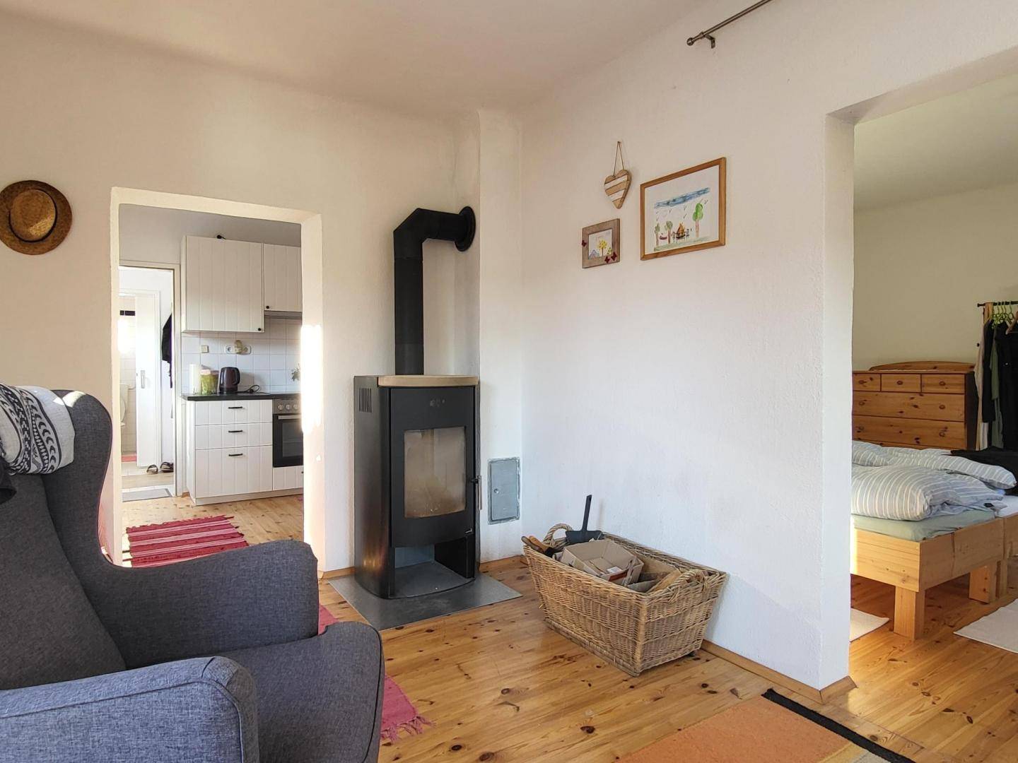 Gemütliches Wohnzimmer mit Holzofen, Holzboden und Blick in die Küche und ein Schlafzimmer.