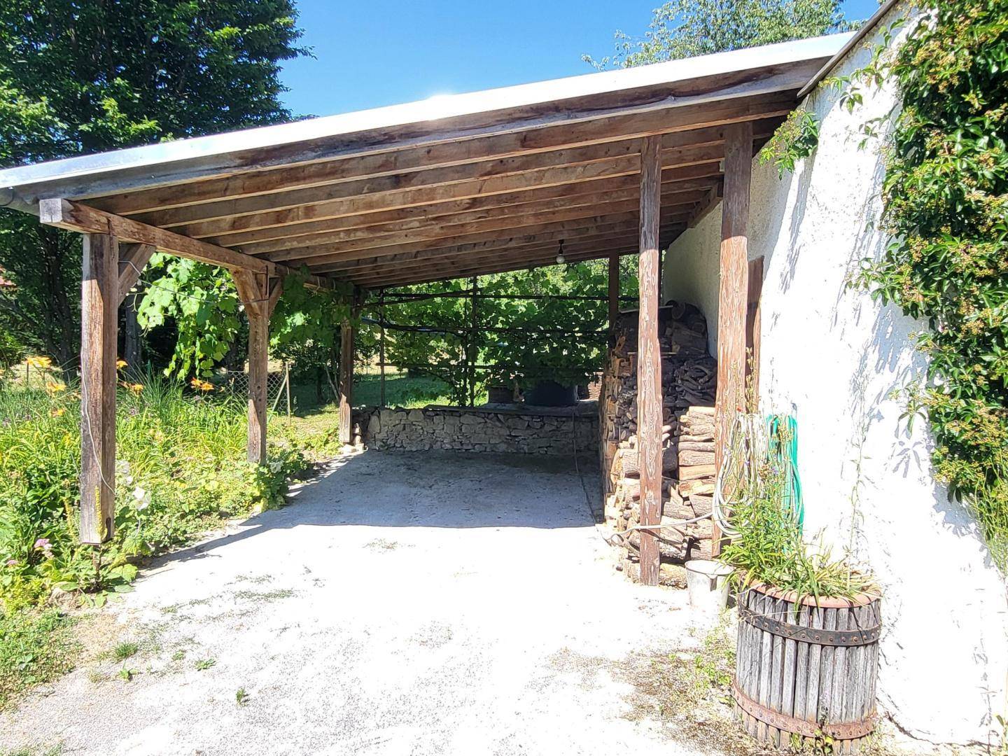 Überdachter Holzcarport neben einem weißen Gebäude mit gestapeltem Brennholz.