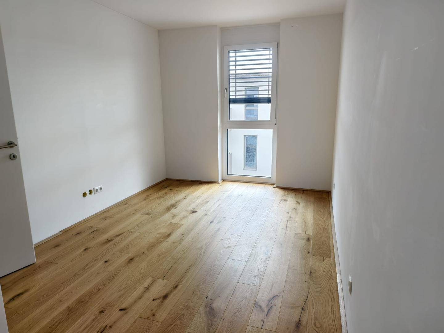 Leeres Schlafzimmer mit hellem Holzboden und einem großen Fenster für viel Tageslicht.