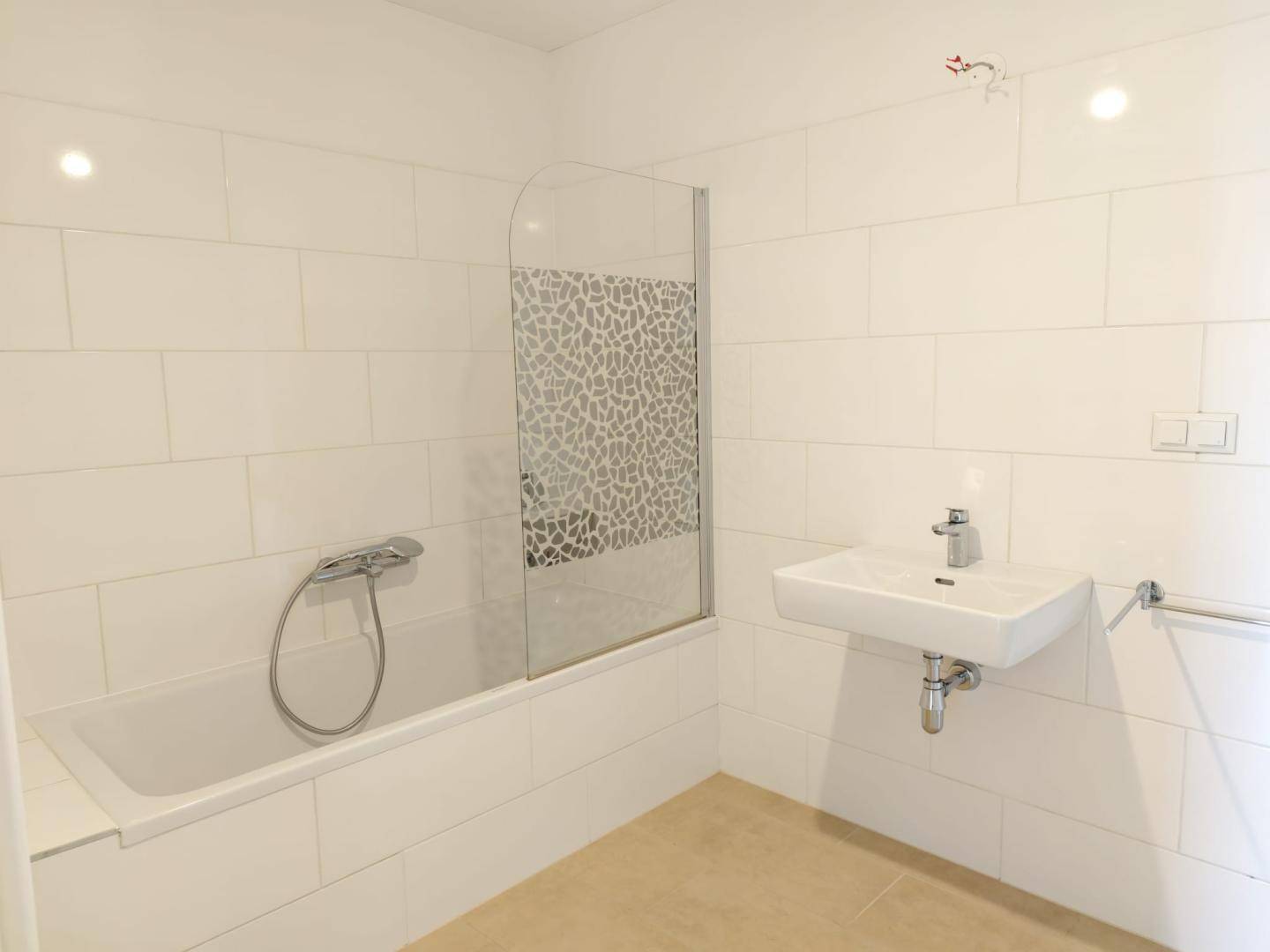 Helles Badezimmer mit weißen Fliesen, Badewanne mit Duschwand und modernem Waschbecken.