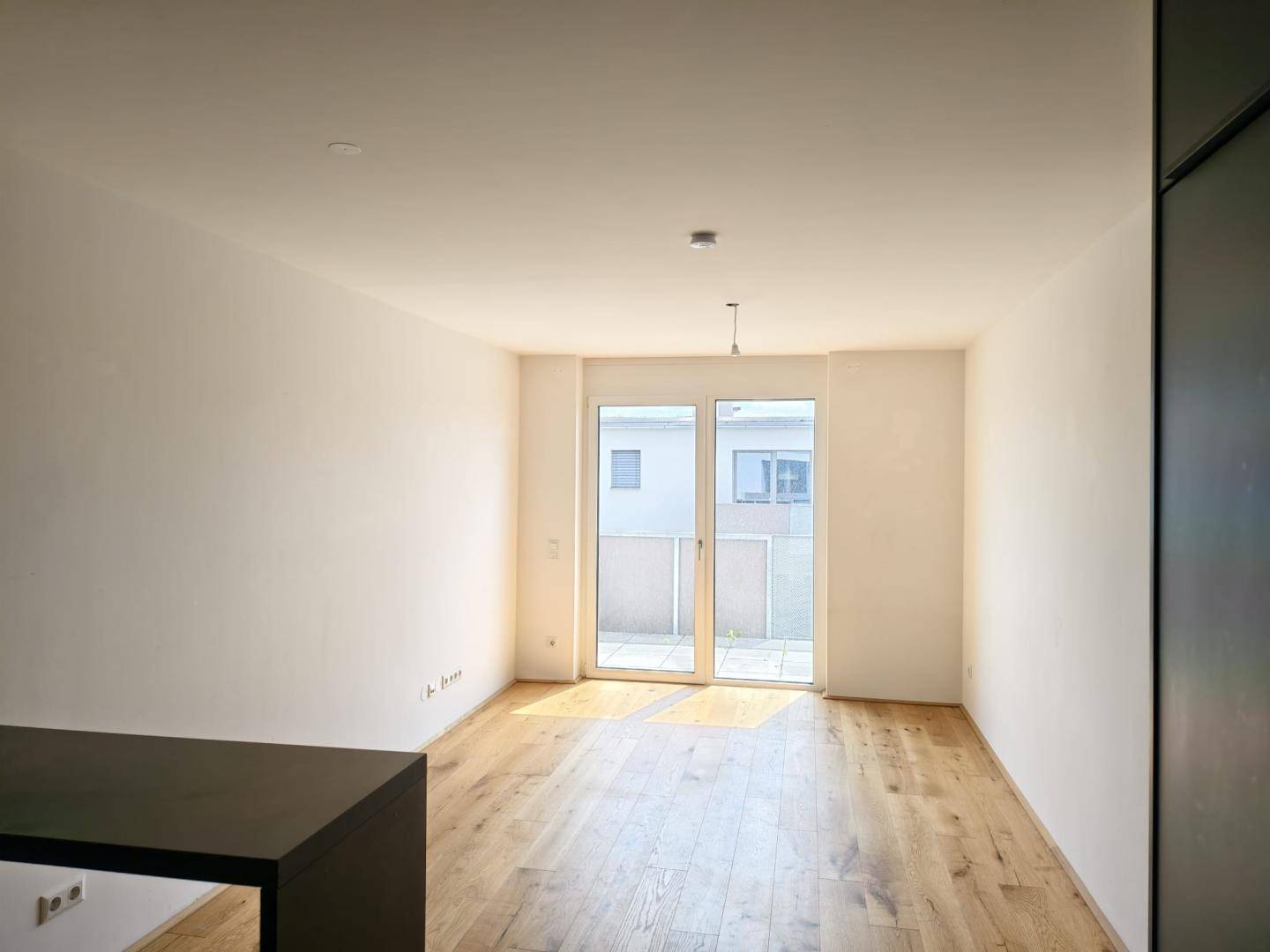 Heller, leerer Raum mit Holzboden und Zugang zu einem Außenbereich durch eine Glastür.
