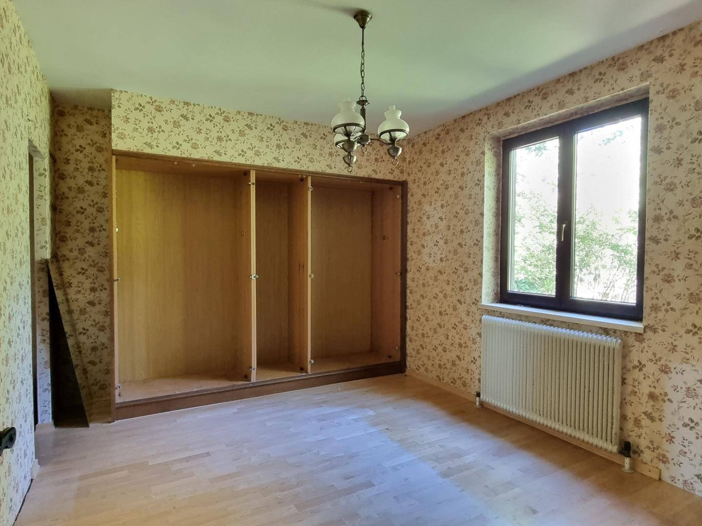 Schlafzimmer mit floraler Tapete, Einbauschränken und hellem Holzboden.