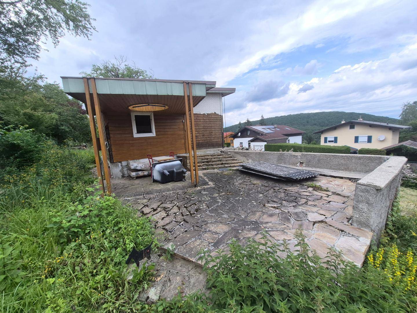 Außenbereich mit kleiner Holzhütte, gepflasterter Fläche und einem leeren Poolbecken im Garten.