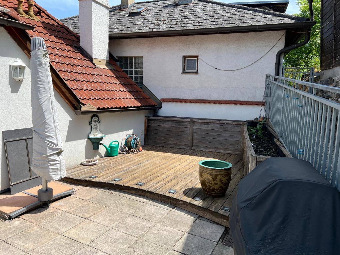 Terrasse mit Holzdeck und gepflastertem Bereich, ausgestattet mit einem Wandbrunnen und Grill.