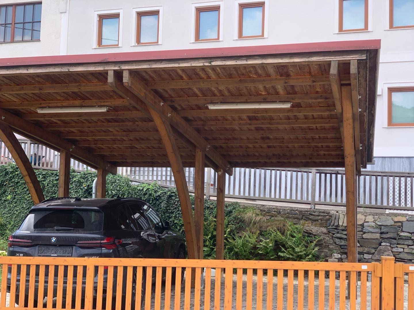 Holz-Carport mit zwei Stellplätzen und einem geparkten Fahrzeug.