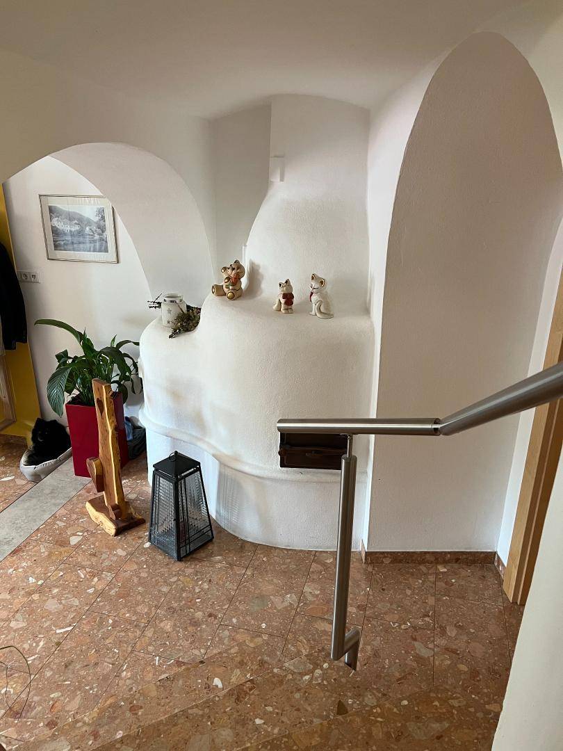 Detailansicht des weißen Kachelofens im Flur mit Terrakotta-Fliesenboden und Dekoration.