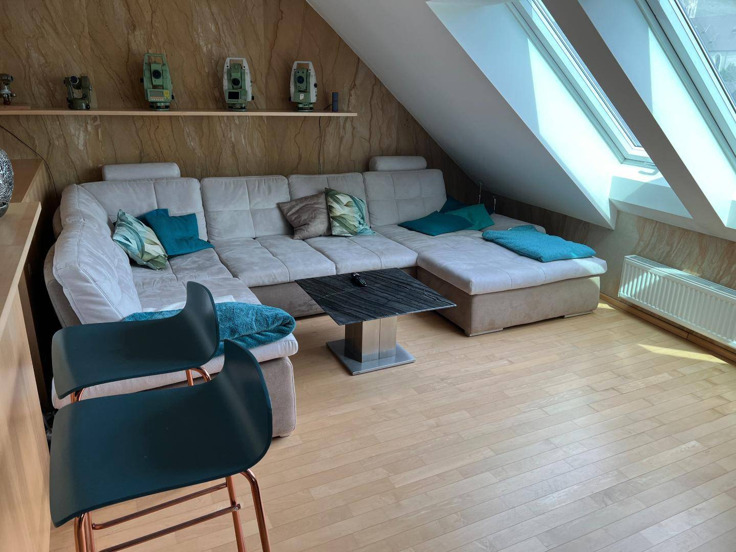 Gemütliches Wohnzimmer im Dachgeschoss mit großem Ecksofa, Holzboden und hellen Dachfenstern.