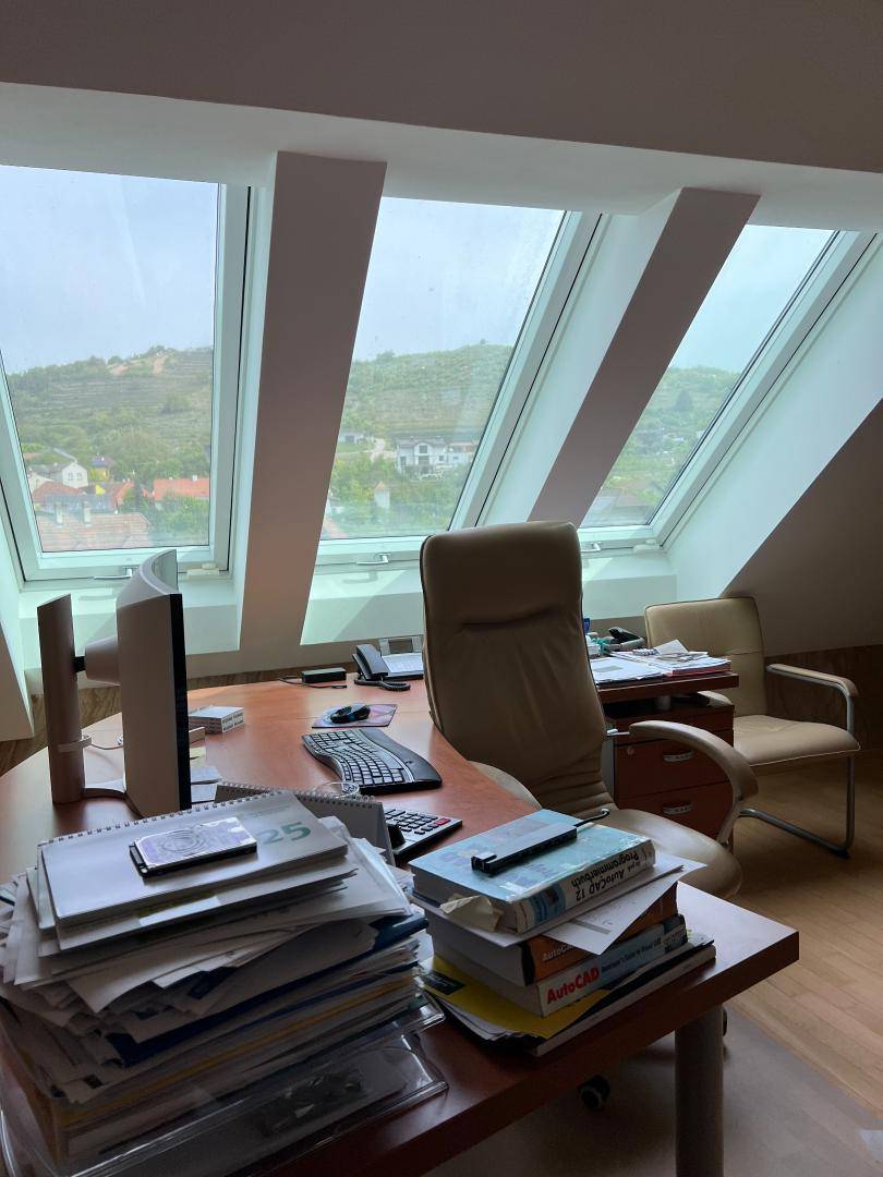Helles Büro im Dachgeschoss mit Schreibtisch, Bürostuhl und weitem Blick auf die umliegende Landschaft.