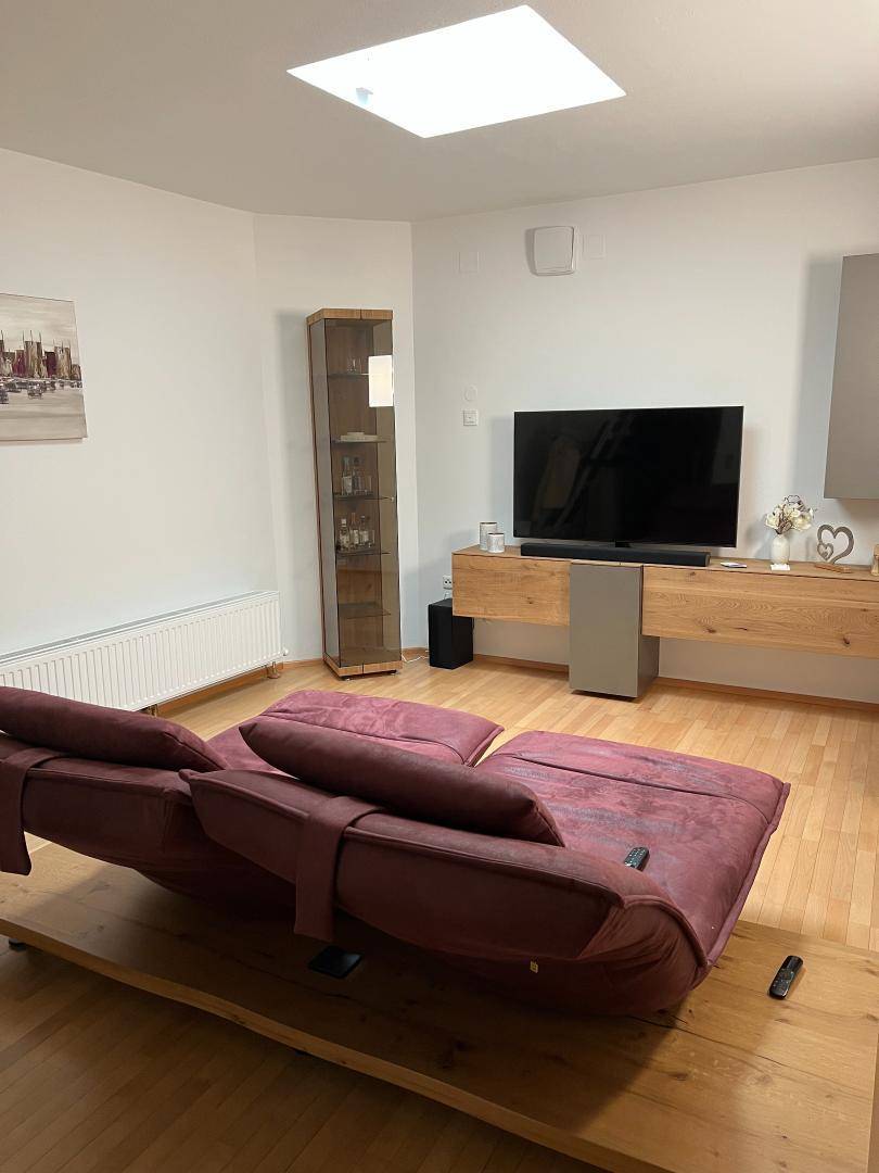 Helles Wohnzimmer mit Holzboden, großem Fernseher und bequemen Liegesofas.
