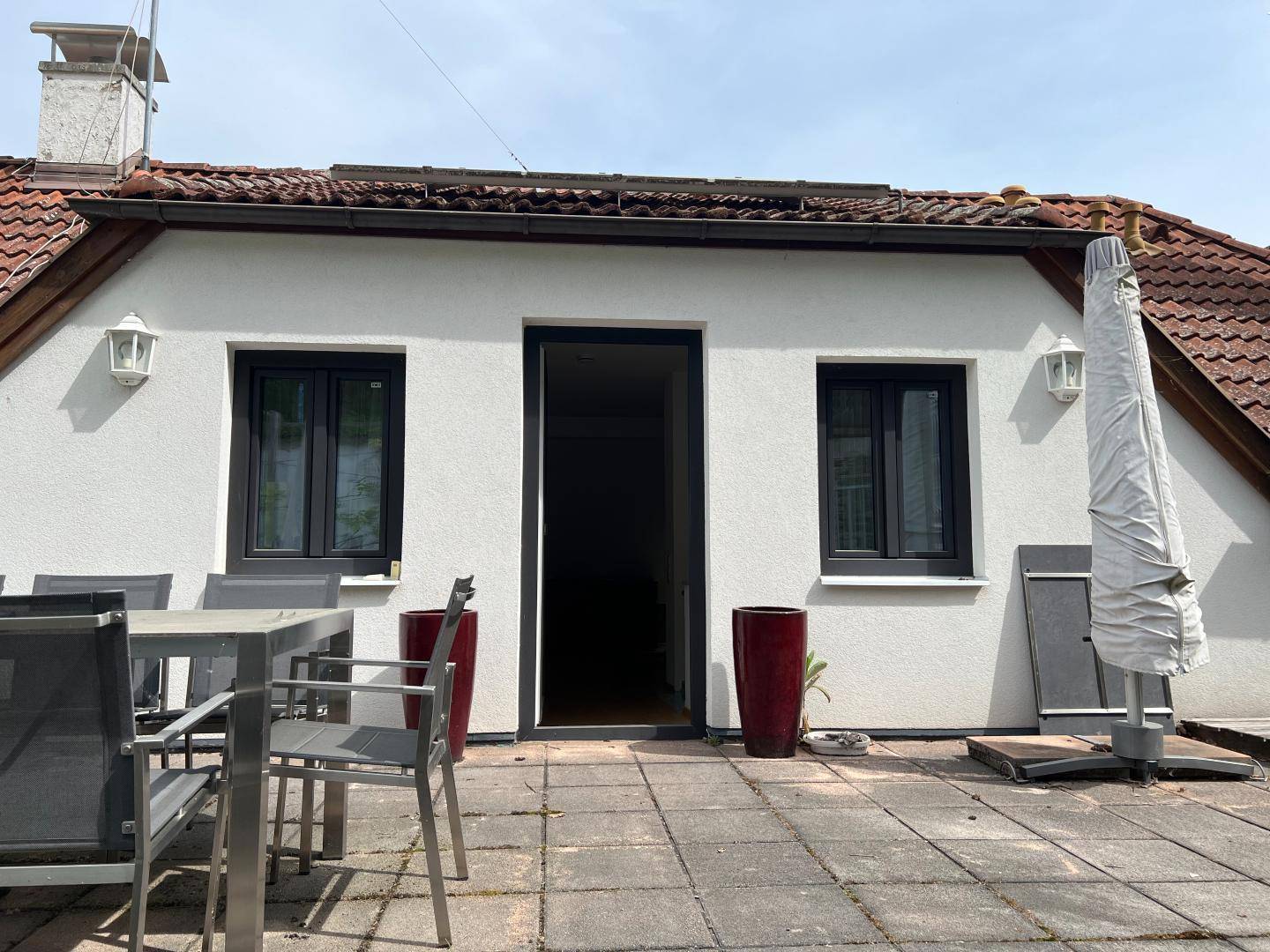 Sonniger Terrassenbereich mit Esstisch, Sonnenschirm und Zugang zum Innenbereich des Hauses.