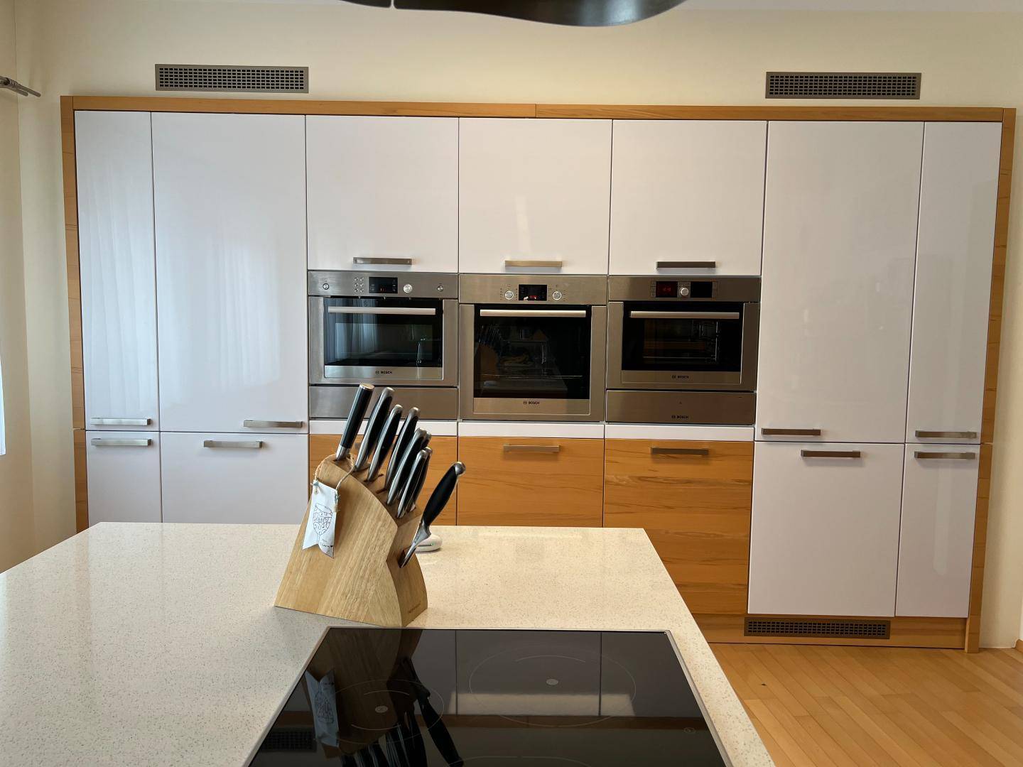 Moderne Einbauküche mit weißen Hochglanzfronten, Holzrahmen und integrierten Öfen.