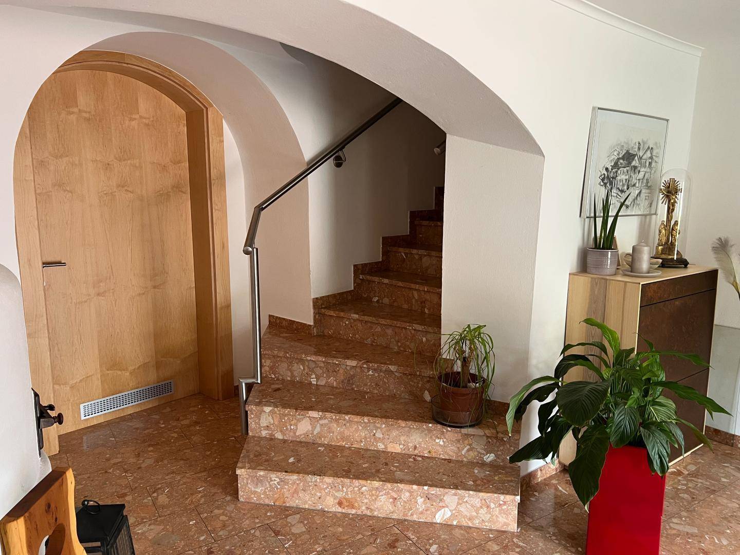 Geräumiger Flur mit Marmortreppe, Terrakotta-Fliesenboden und Holz-Rundbogentür.