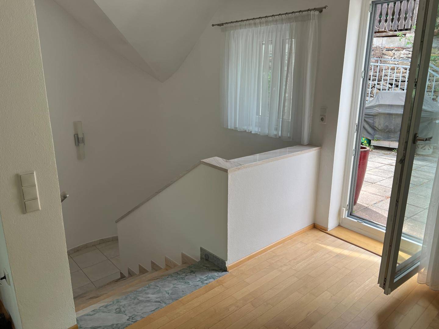 Heller Flur mit Treppenaufgang, Fenster und direktem Zugang zu einer Außenterrasse.