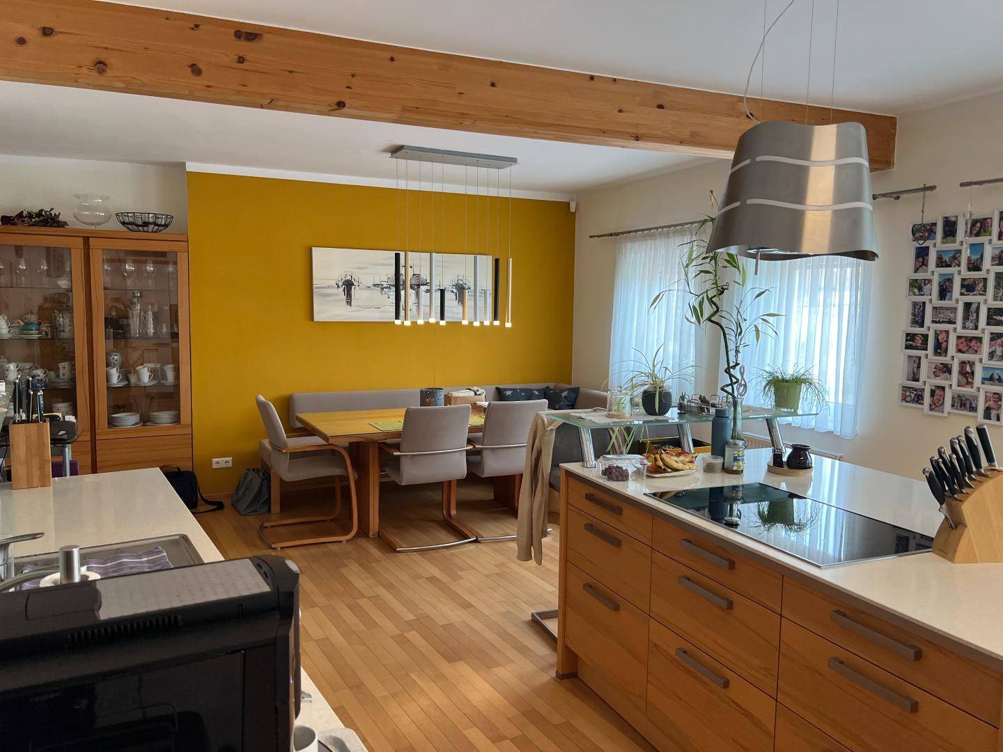 Offene Küche mit Essbereich, Holzbalken und gelber Akzentwand.