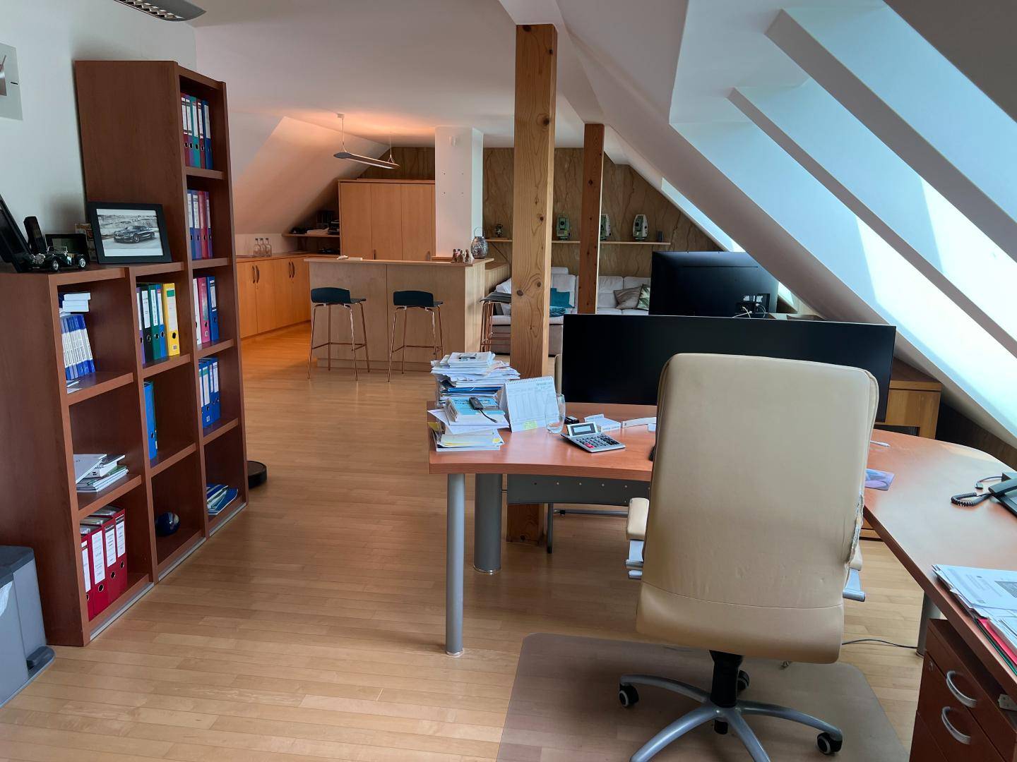 Offener Dachgeschossbereich mit Büroecke, Bücherregalen und einer kleinen Küchenzeile im Hintergrund.