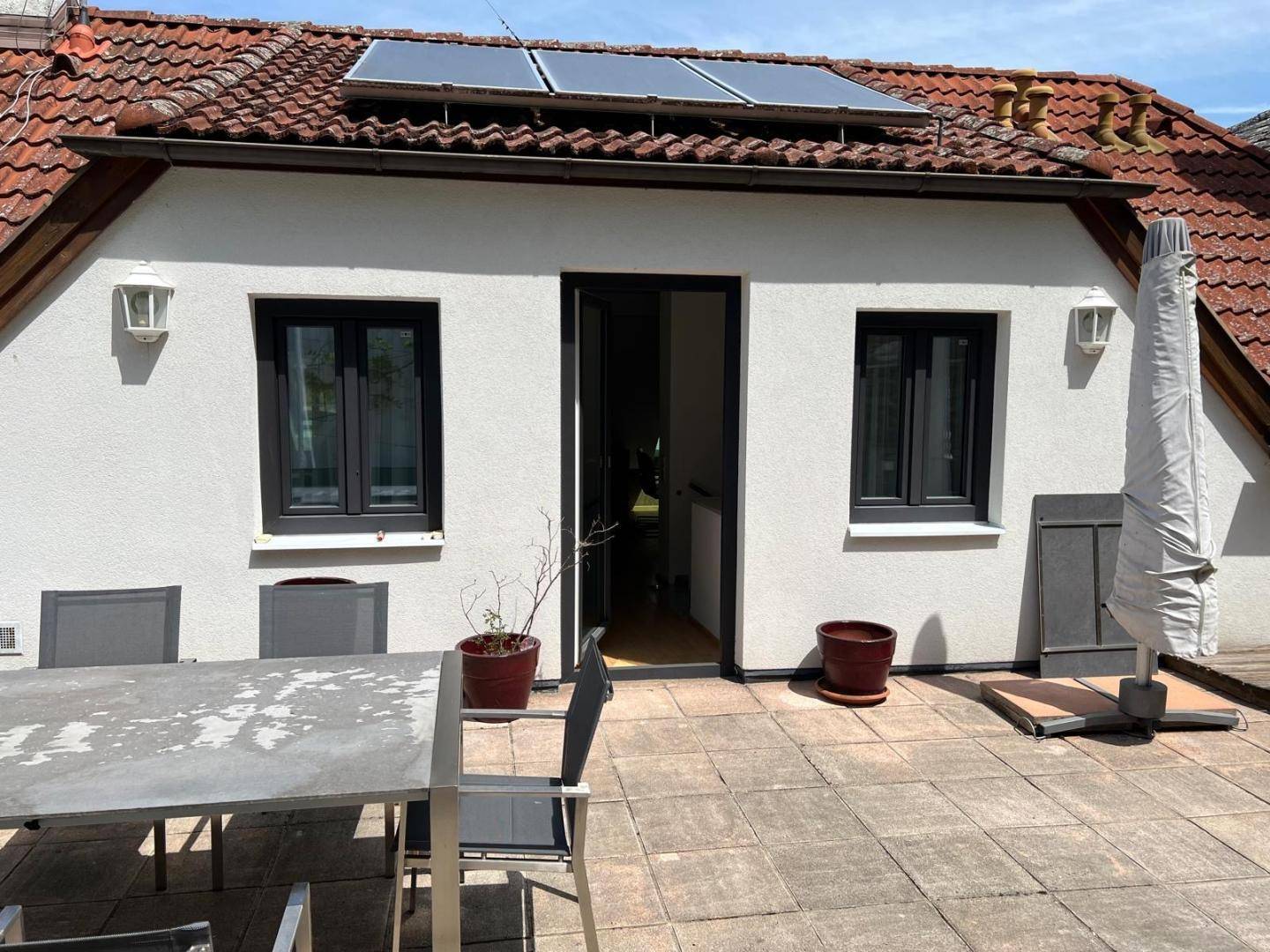 Sonniger Terrassenbereich mit Esstisch, Sonnenschirm und Zugang zum Innenbereich des Hauses.