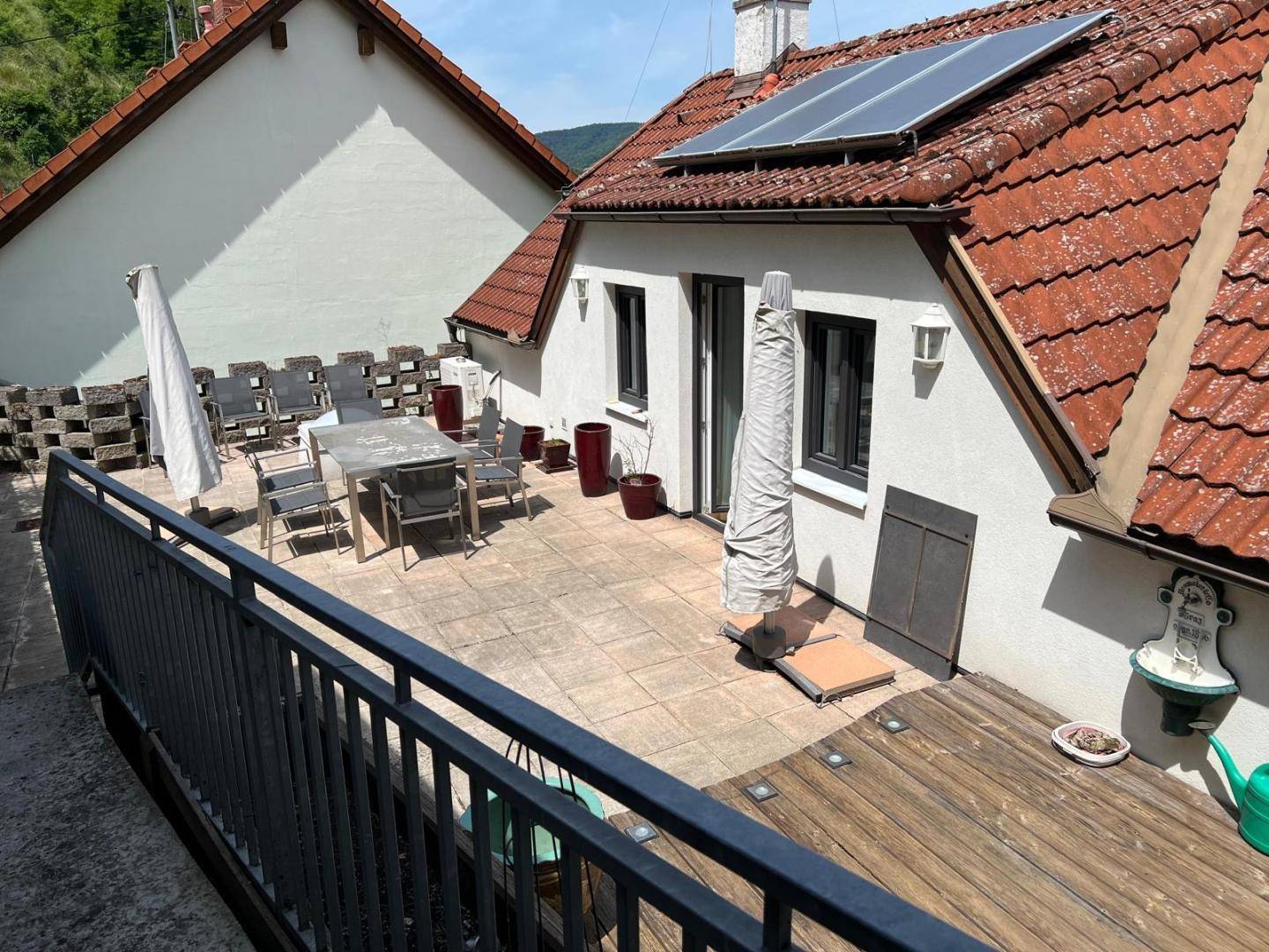 Große Terrasse mit gepflastertem Bereich und Holzdeck, umgeben von einer Metallbrüstung und Bergblick.