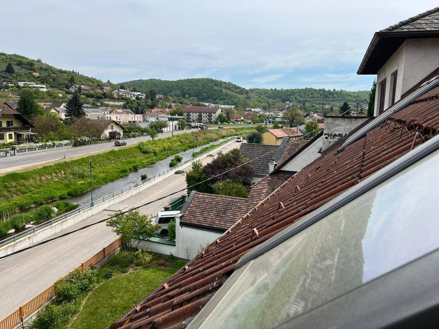 Ausblick über Dächer, eine Straße, einen Fluss und die umliegende grüne Hügellandschaft.