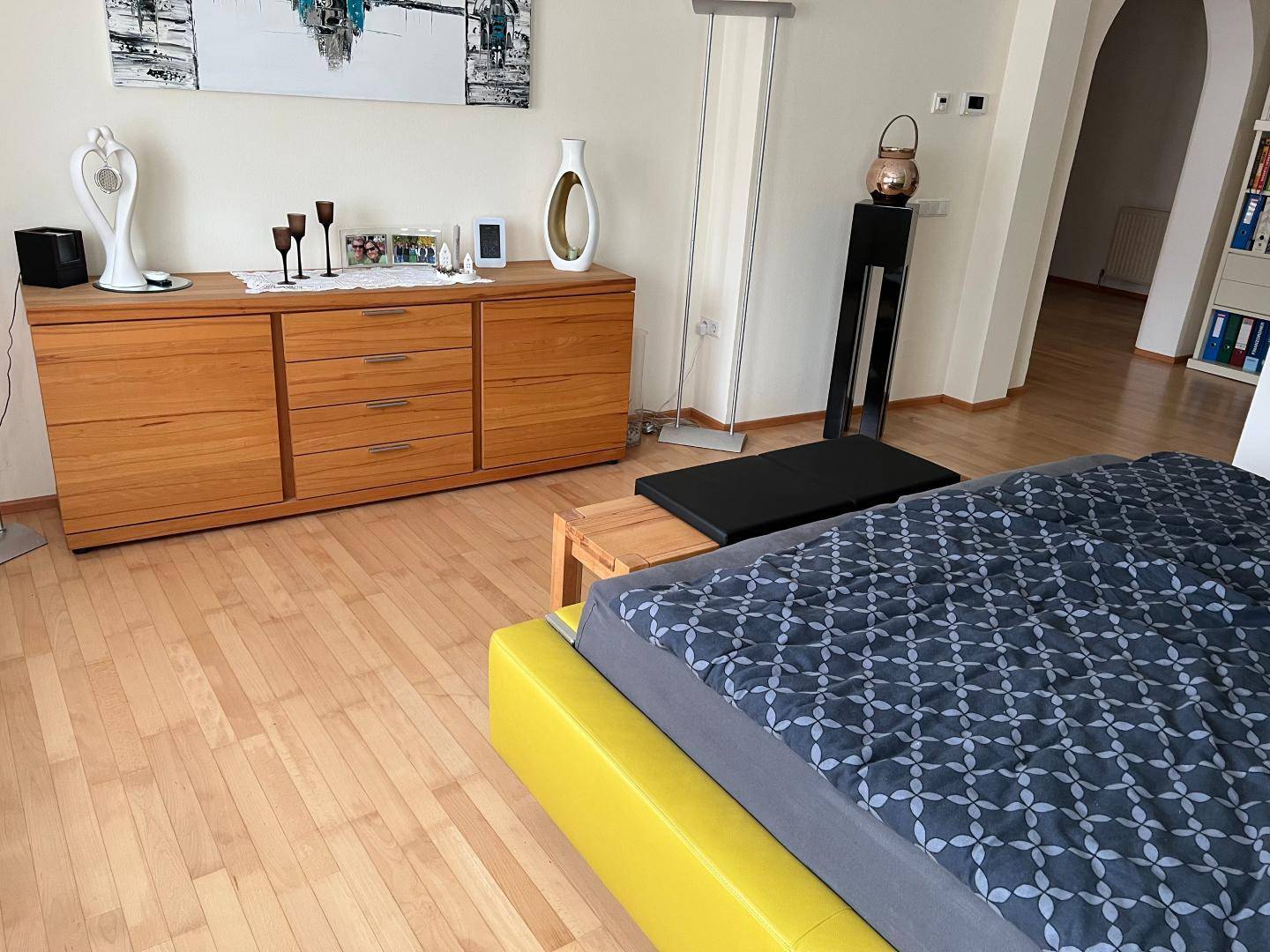 Helles Schlafzimmer mit Holzboden, Kommode und modernem Doppelbett.