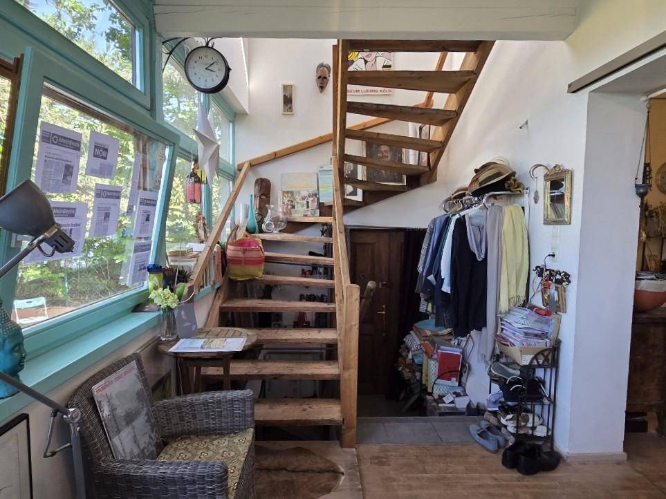 Flur mit Holztreppe, die in die obere Etage führt, und großen Fenstern.