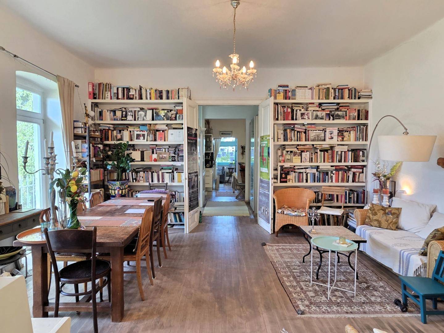 Geräumiger Wohn- und Essbereich mit Holzboden, Bücherregalen und Kronleuchter.