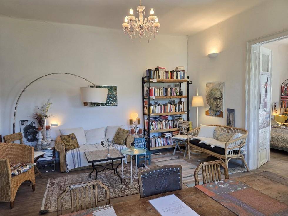 Gemütlicher Wohnbereich mit Sofa, Rattansesseln, Bücherregal und Kronleuchter.