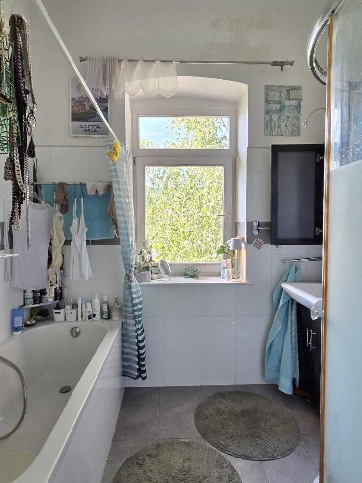 Helles Badezimmer mit Badewanne, Dusche und Fenster mit Blick ins Grüne.