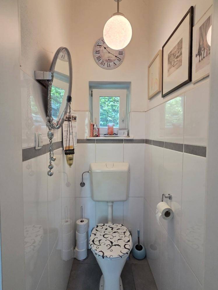 Kleines Gäste-WC mit Fenster, WC und Spiegel, hell gefliest.