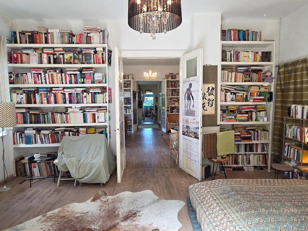 Schlafzimmer mit Bücherregalen an den Wänden und Blick durch eine offene Tür in den Flur.