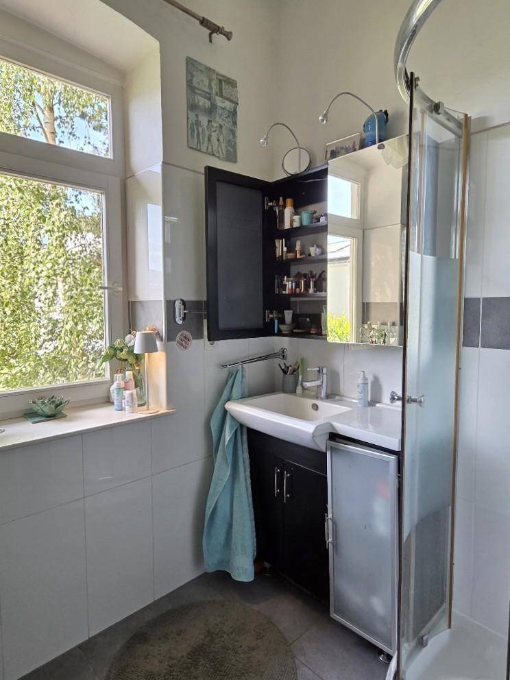 Badezimmer mit Waschbecken, Spiegelschrank und Duschkabine, hell durch ein Fenster.