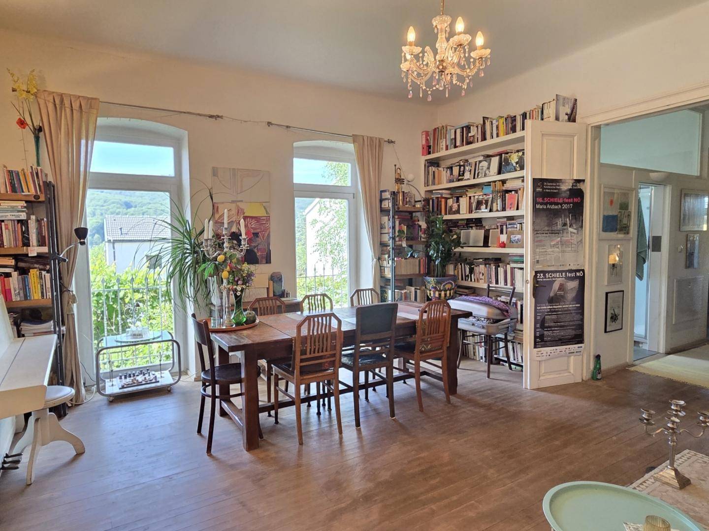 Heller Wohn- und Essbereich mit Holzboden, großem Esstisch und Bücherregalen.