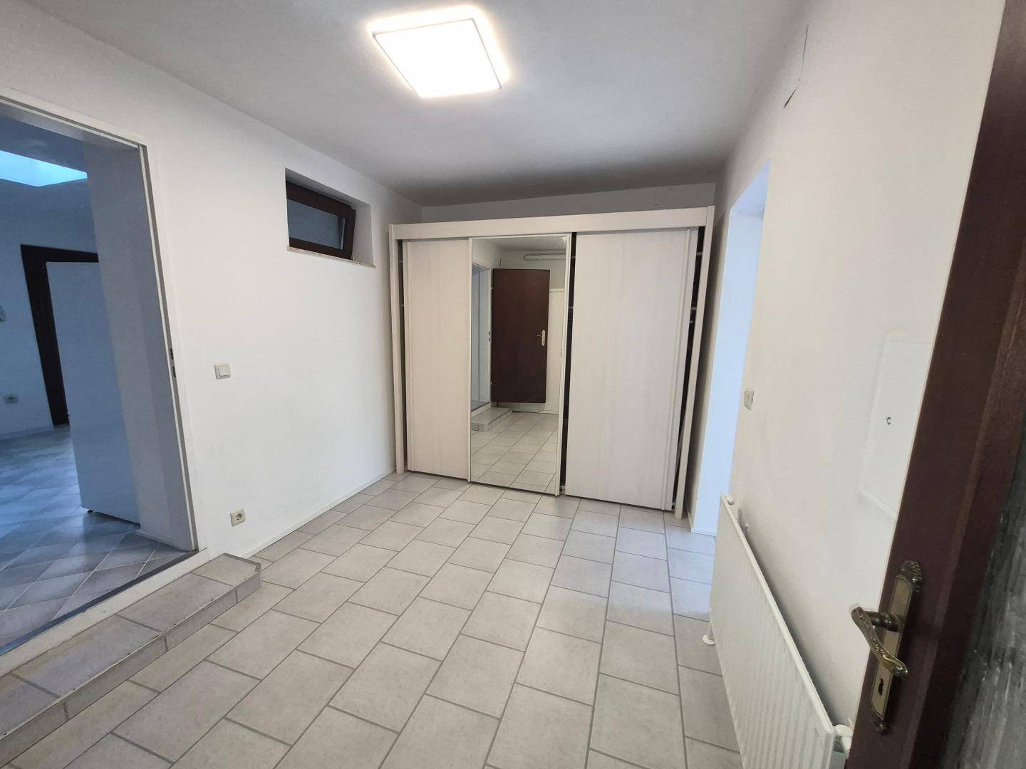 Flur mit Fliesenboden, einem großen Einbauschrank mit Spiegeltüren und Zugang zu weiteren Zimmern.