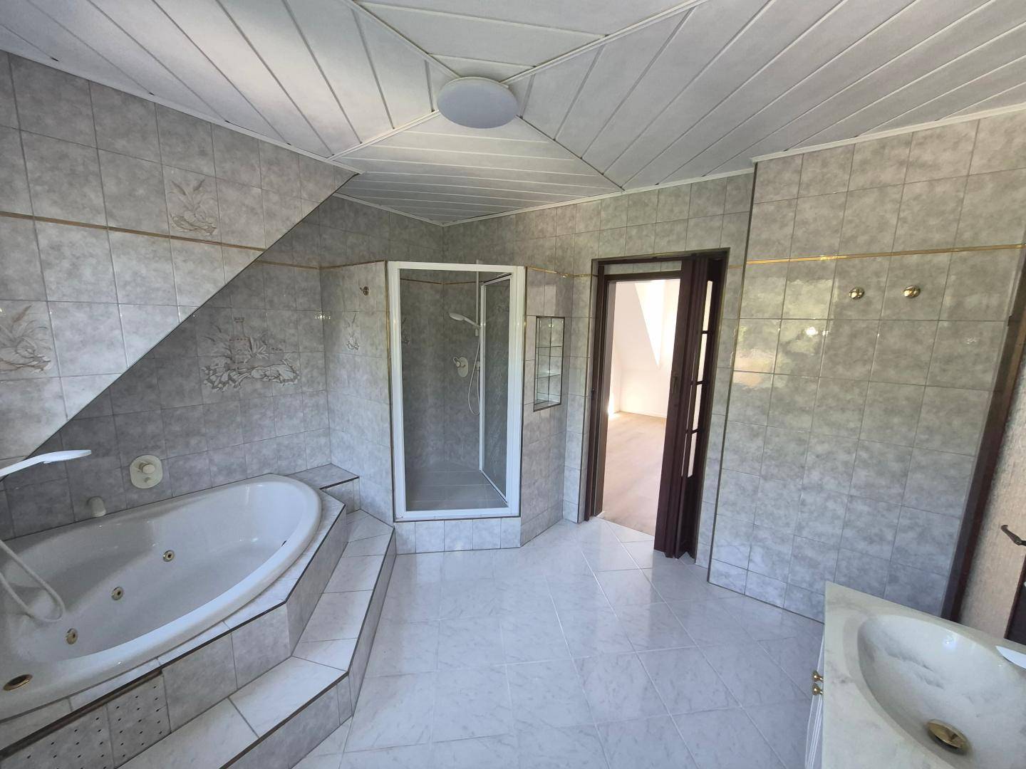 Geräumiges Badezimmer mit Fliesen, Eckbadewanne, Duschkabine und Zugang zu einem weiteren Raum.