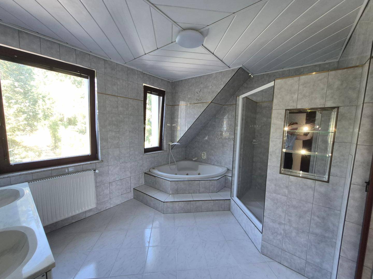 Gefliestes Badezimmer mit Eckbadewanne, Duschkabine und zwei Fenstern für natürliche Belüftung.