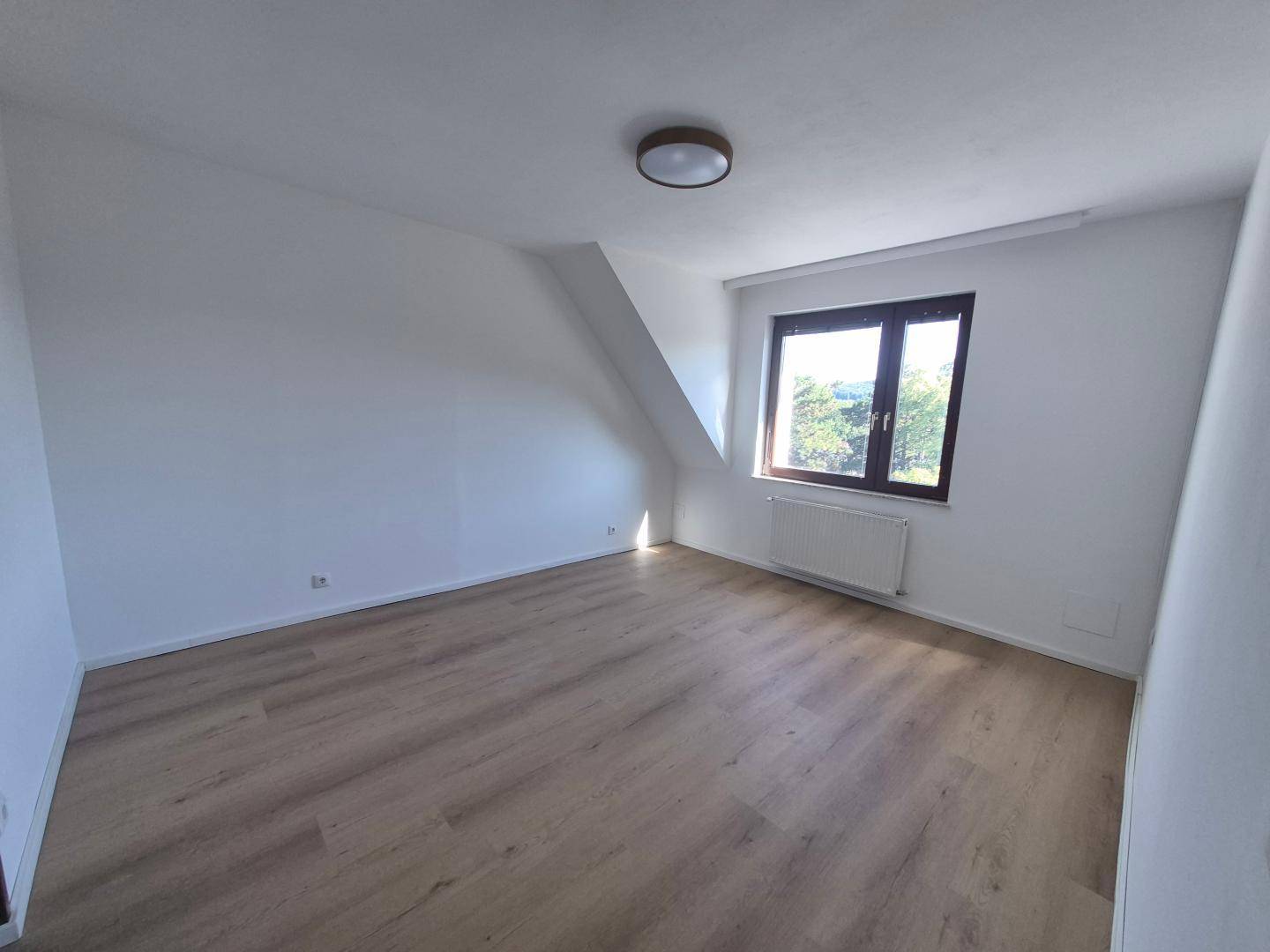Helles Schlafzimmer mit Laminatboden, Dachschräge und Fenster mit Blick auf die Umgebung.